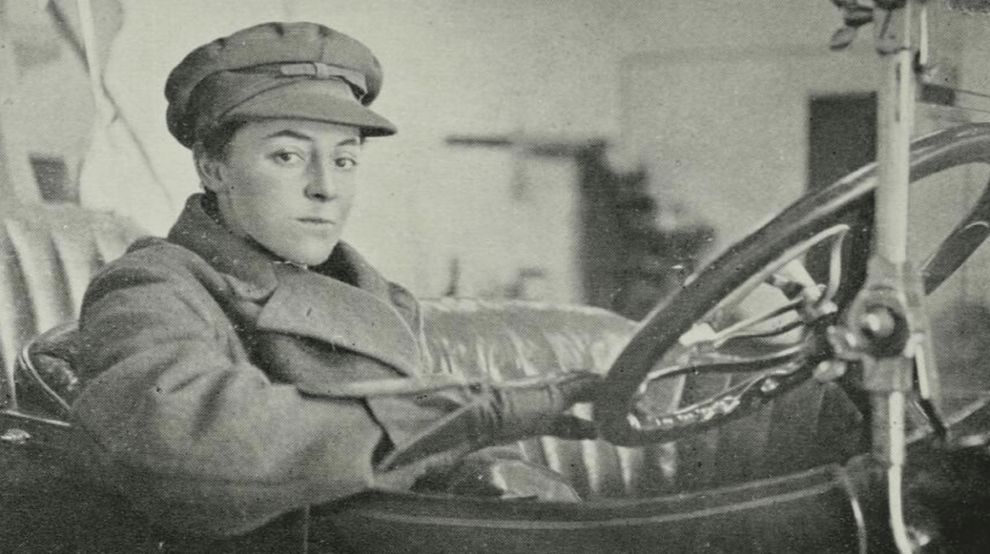 Photograph Alice Anderson. She is sitting in the driver's seat of a car and is holding the steering wheel.
